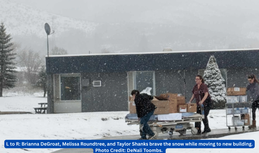 Three people skateboarding on a snowy day outside a blue building.
