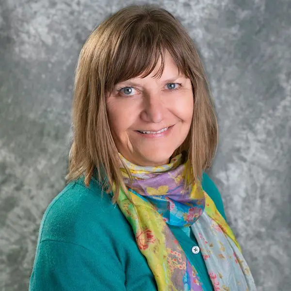 A woman with brown hair wearing a blue jacket and colorful scarf.