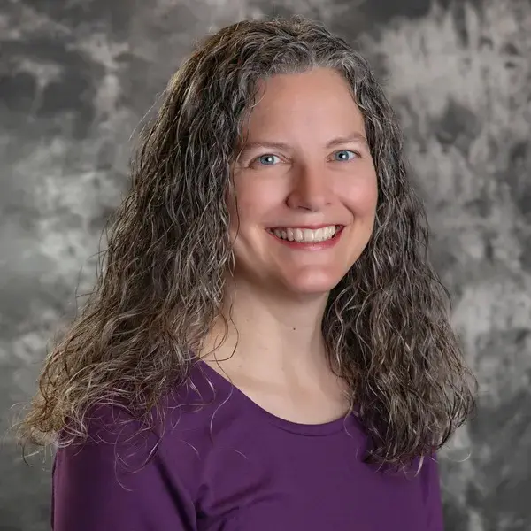 A woman with long hair and purple shirt smiling.