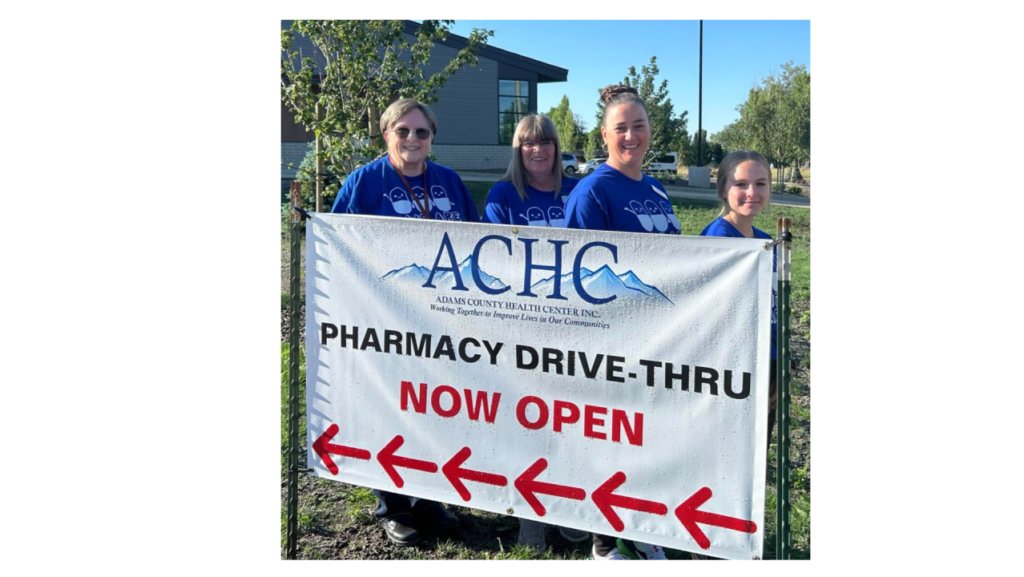 Four women standing next to a sign that says pharmacy drive-thru.