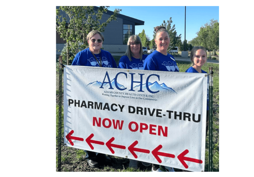 Four women standing next to a sign that says pharmacy drive-thru.